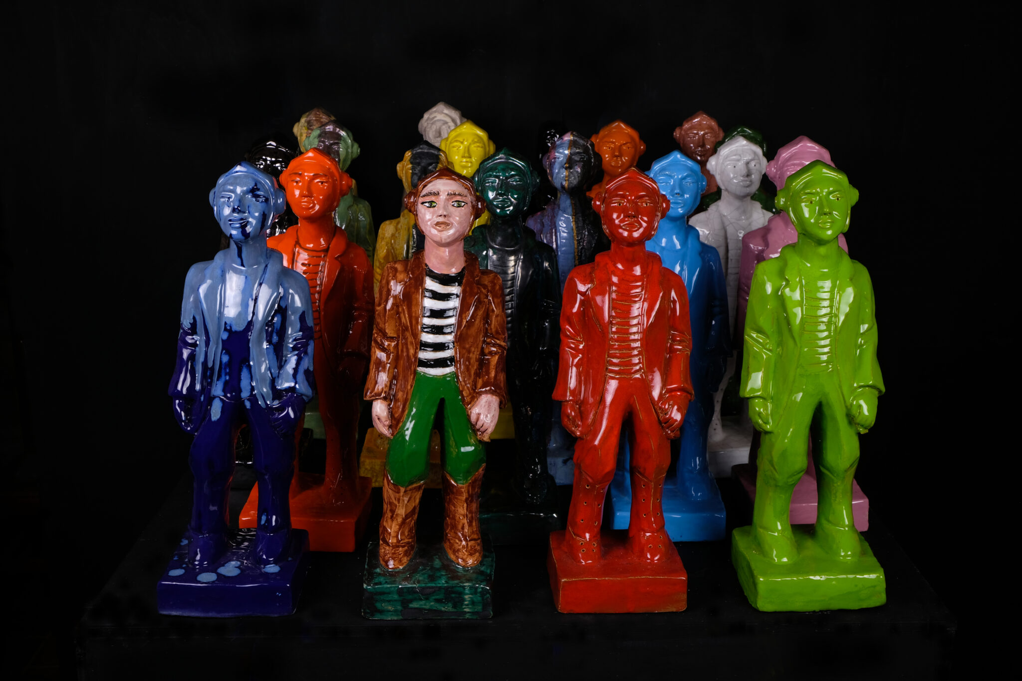 Viele hintereinander stehende Keramikfiguren, die einen Piloten darstellen mit verschiedenfarbigen, knallbunten Glasuren
