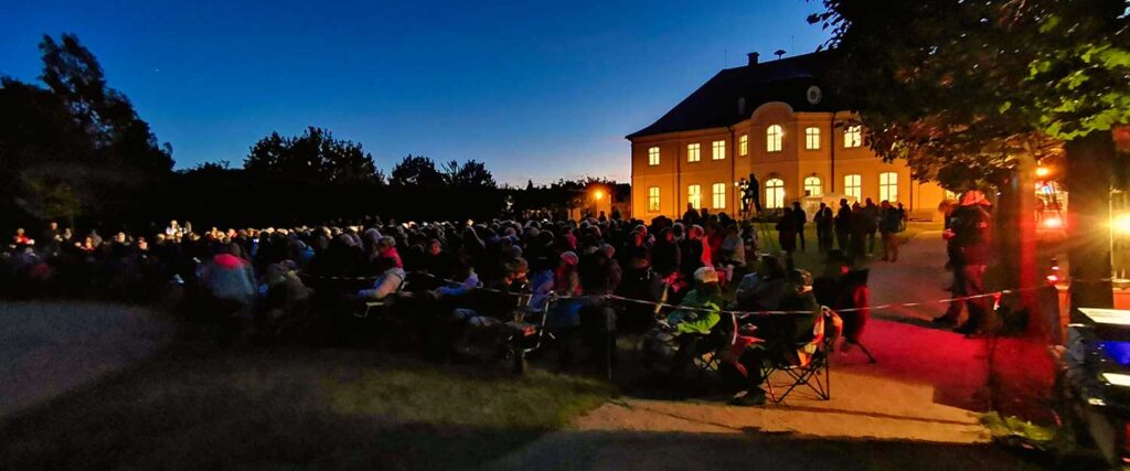 Publikum am Abend vor einem beleuchteten Schloss